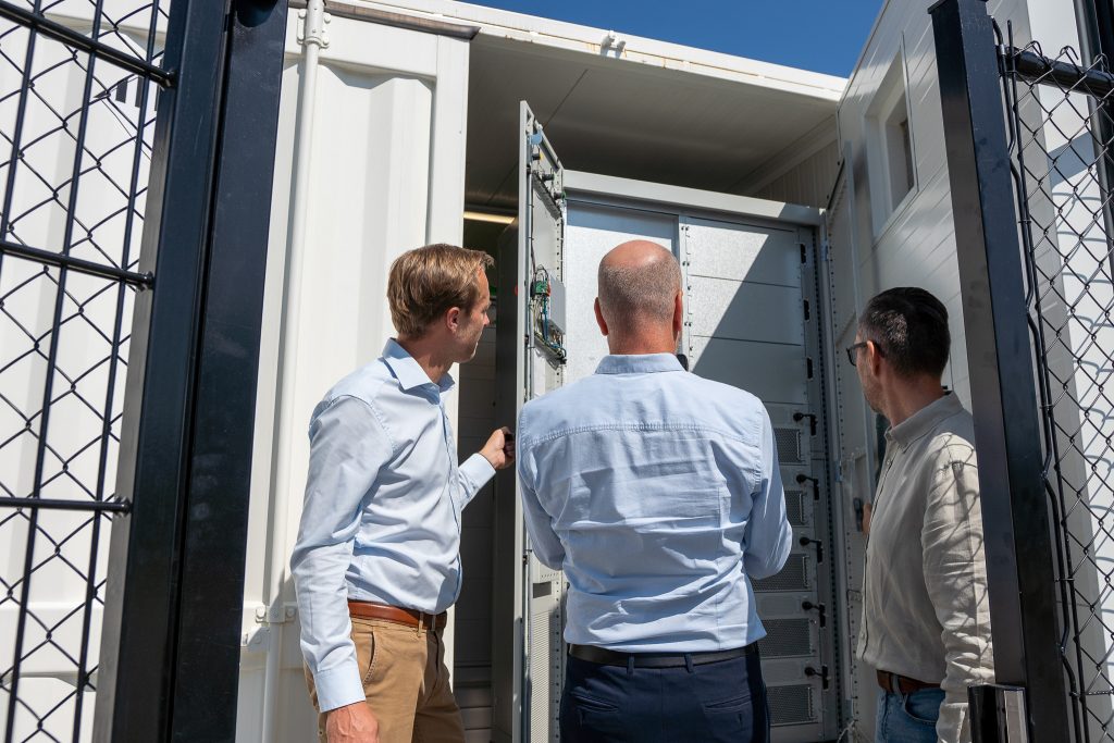 three men looking inside a battery container